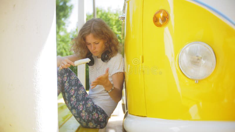 Mujer joven al aire libre por música que escucha del coche amarillo del carro en auriculares usando el smartphone - relajación, g