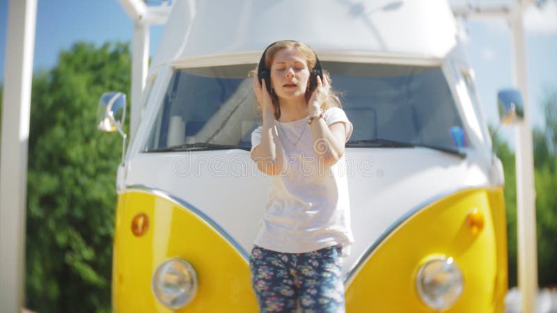 Mujer joven al aire libre por música que escucha del coche amarillo del carro en auriculares usando el smartphone - relajación, g