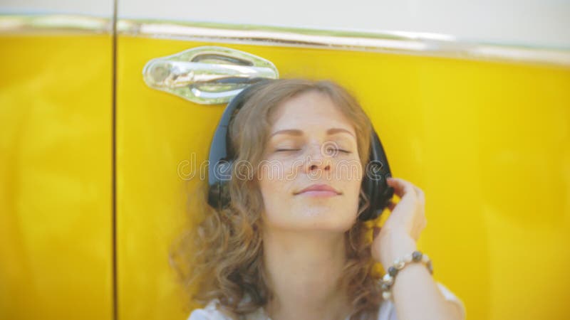 Mujer joven al aire libre por música que escucha del coche amarillo del carro en auriculares usando el smartphone - relajación, g