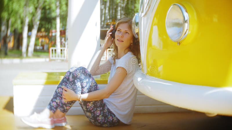 Mujer joven al aire libre por música que escucha del coche amarillo del carro en auriculares usando el smartphone - relajación, g