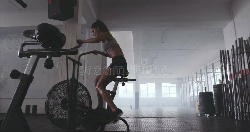 Mujer joven apta que usa la bicicleta estática en el gimnasio