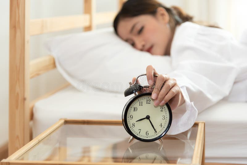 Mujer joven asi?tica de la belleza que apaga el despertador por ma?ana tarde sin la mirada del reloj y perezoso al trabajo encend imagen de archivo libre de regalías Mujer joven asi?tica de la belleza que apaga el despertador por ma?ana tarde sin la mirada del reloj y perezoso al trabajo encend imagen de archivo libre de regalías