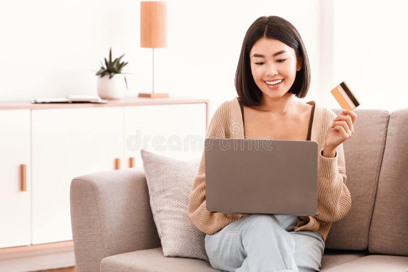 Mujer joven asiática haciendo compras sentada con un pc en el sofá fotos de archivo