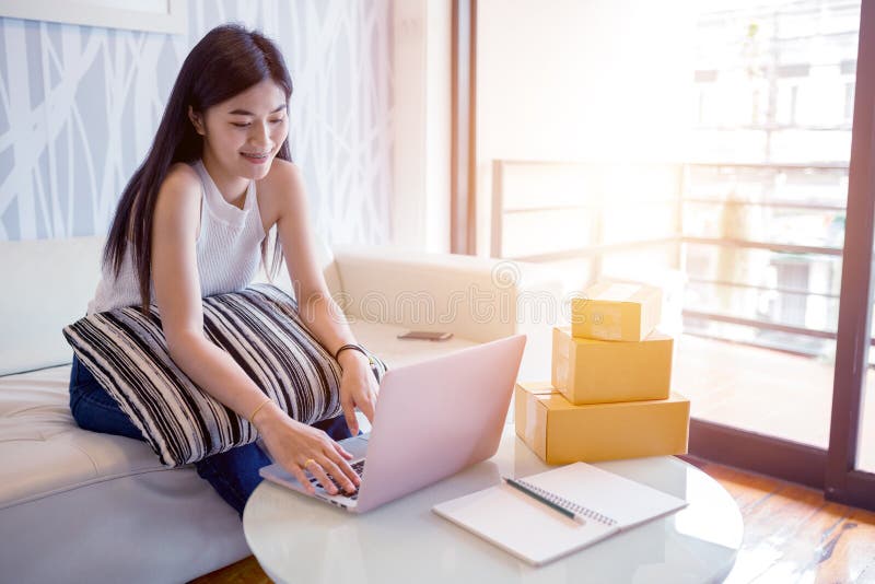 Mujer joven asiática que usa el ordenador portátil que comprueba el producto de la orden imágenes de archivo libres de regalías Mujer joven asiática que usa el ordenador portátil que comprueba el producto de la orden imágenes de archivo libres de regalías