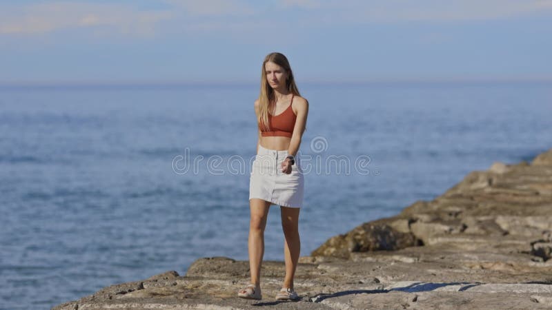 Mujer joven caminando sobre un rompeolas cerca del mar almacen de metraje de vídeo