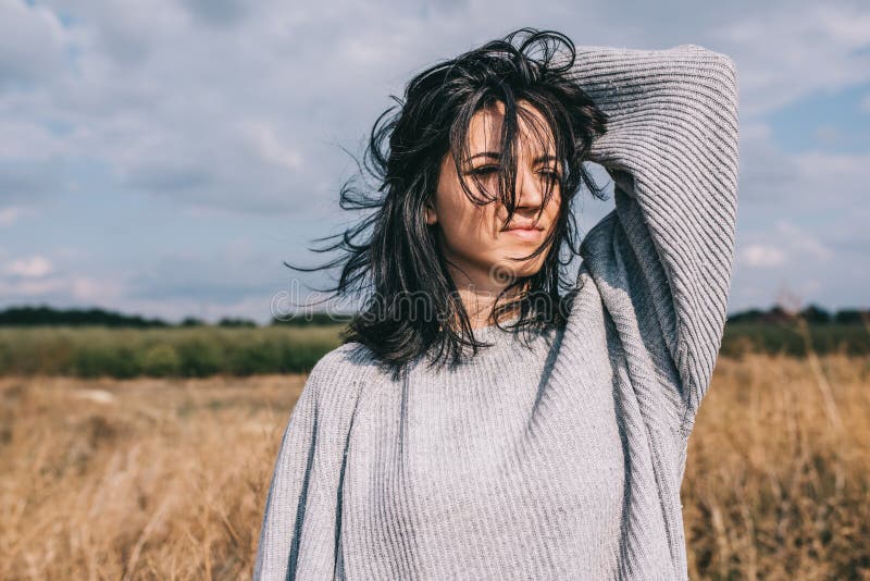 Mujer joven caucásica morena con el exterior ventoso del pelo que sopla, contra prado y el cielo Retrato de la hembra ideal que m imágenes de archivo libres de regalías Mujer joven caucásica morena con el exterior ventoso del pelo que sopla, contra prado y el cielo Retrato de la hembra ideal que m imágenes de archivo libres de regalías