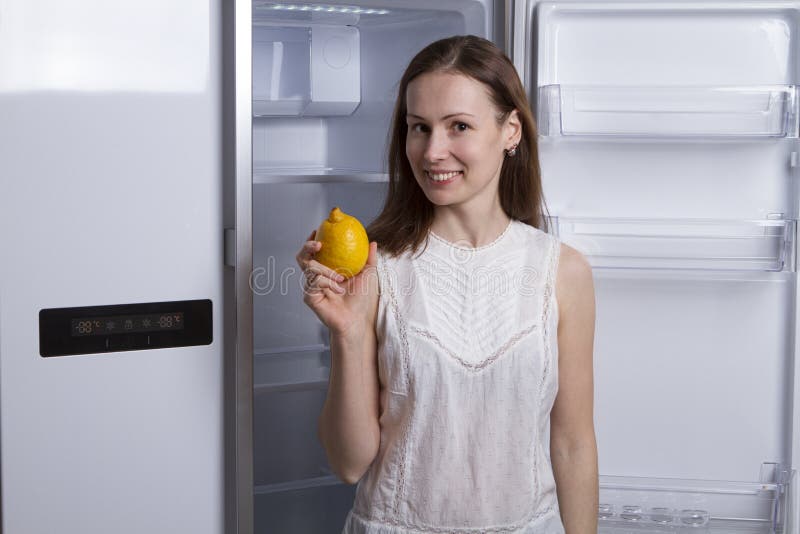 Mujer joven cerca del refrigerador vacío con la fruta imagen de archivo Mujer joven cerca del refrigerador vacío con la fruta imagen de archivo