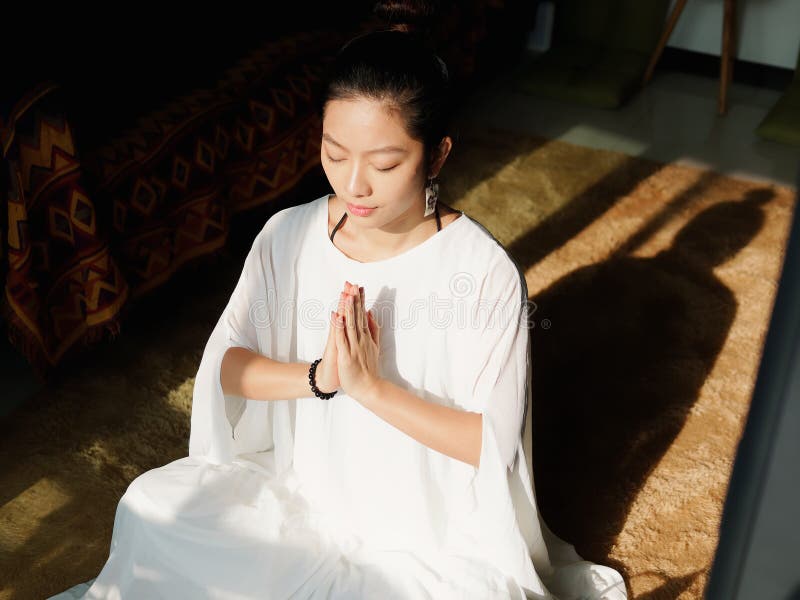 Mujer joven china bonita que medita en casa, sentándose en piso con el amortiguador peludo en luz del sol imagen de archivo Mujer joven china bonita que medita en casa, sentándose en piso con el amortiguador peludo en luz del sol imagen de archivo
