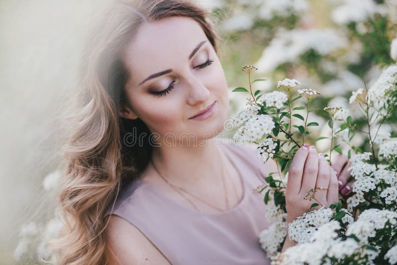 Mujer joven con el pelo hermoso largo en un vestido de la gasa que presenta con el jardín del lilacin con las flores blancas imagenes de archivo Mujer joven con el pelo hermoso largo en un vestido de la gasa que presenta con el jardín del lilacin con las flores blancas imagenes de archivo