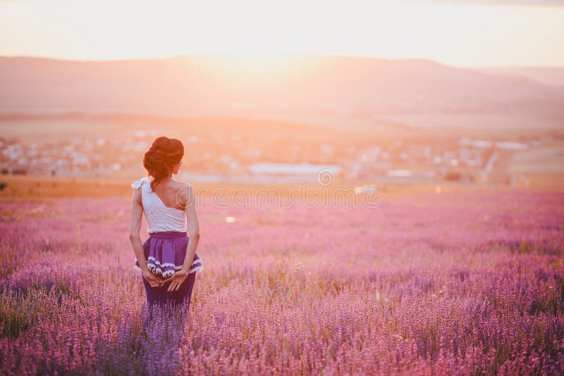 Mujer joven con el pelo hermoso que se coloca en un campo de la lavanda en la puesta del sol fotos de archivo Mujer joven con el pelo hermoso que se coloca en un campo de la lavanda en la puesta del sol fotos de archivo
