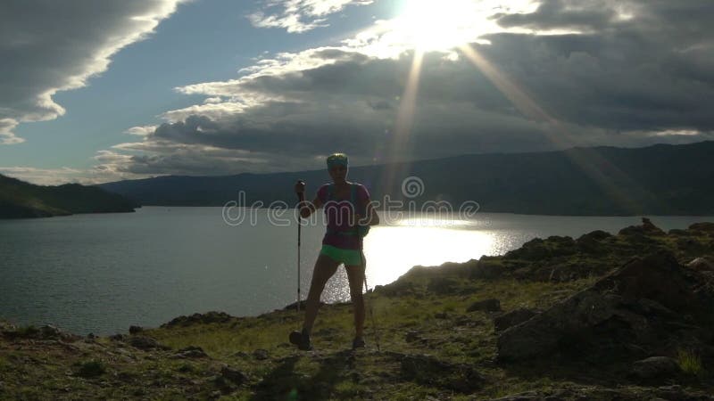 Mujer joven con la mochila que camina alrededor de las montañas y del lago