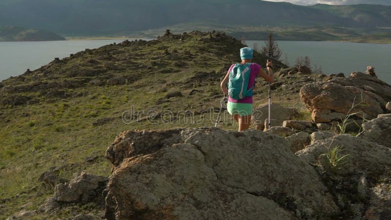 Mujer joven con la mochila que camina alrededor de las montañas y del lago