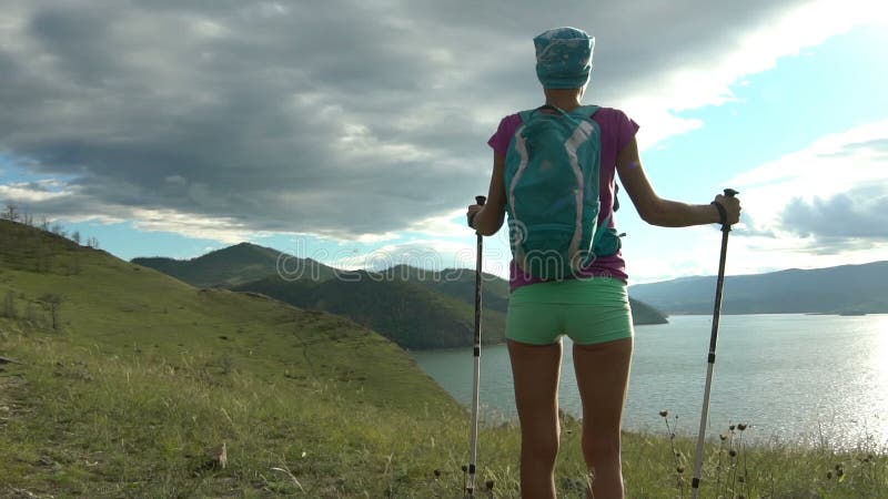 Mujer joven con la mochila que camina alrededor de las montañas y del lago