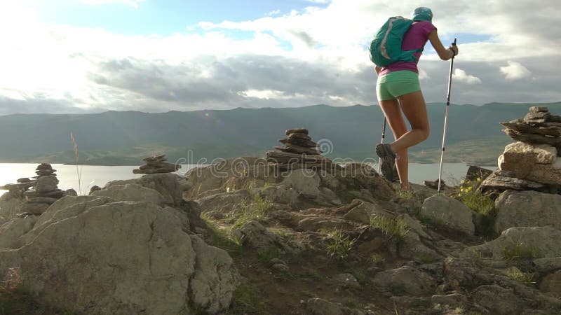 Mujer joven con la mochila que camina alrededor de las montañas y del lago