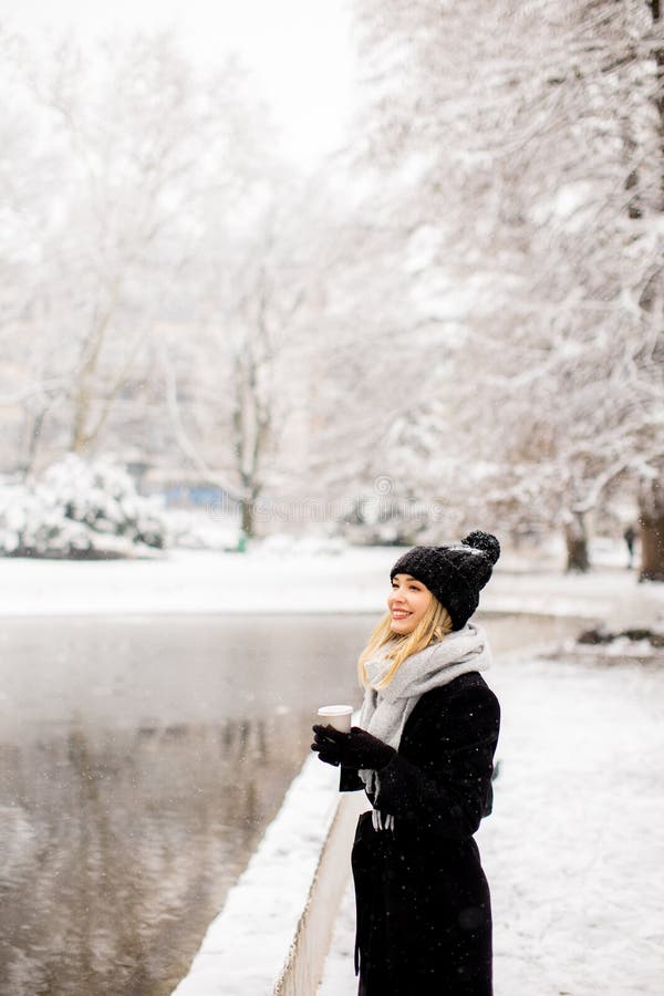 Mujer en ropa de invierno elegante con taza de café al aire libre.