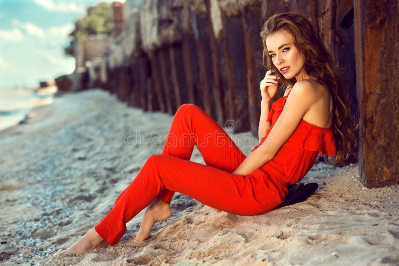 Joven Elegante Encantadora En El Coralino Del Hombro Del Rojo Uno Que Se Sienta En La Playa En Las Pilas Oxidadas Viej Foto de archivo - Imagen de pilas, exterior:
