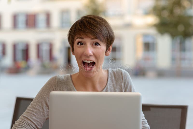 Mujer joven emocionada que reacciona a las noticias en su ordenador portátil fotografía de archivo
