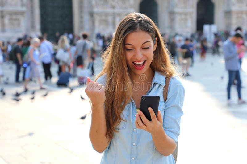 Mujer joven emocionada que recibe buenas noticias en línea en un teléfono elegante imagen de archivo libre de regalías Mujer joven emocionada que recibe buenas noticias en línea en un teléfono elegante imagen de archivo libre de regalías