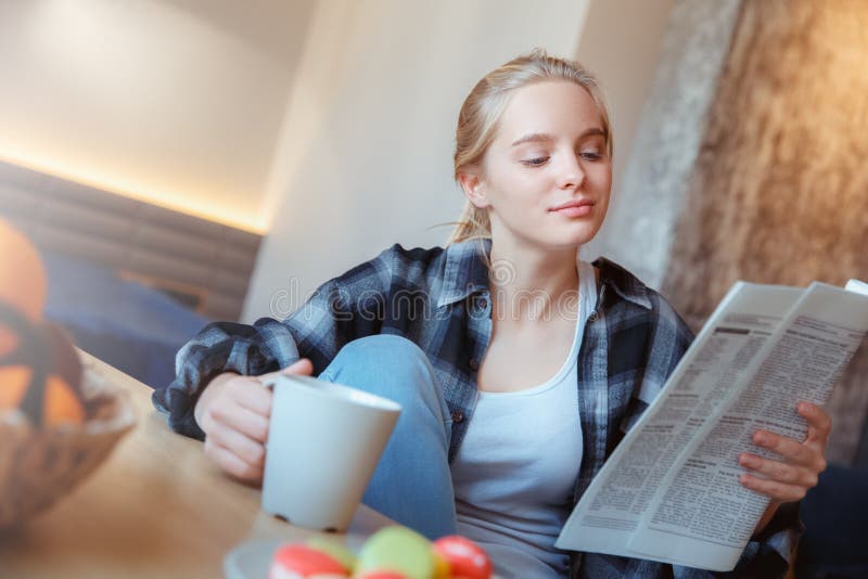 Mujer joven en casa en las noticias de consumición de la lectura del té de la cocina imagenes de archivo Mujer joven en casa en las noticias de consumición de la lectura del té de la cocina imagenes de archivo