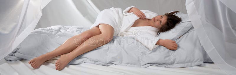 Mujer joven en la albornoz blanca en la cama blanca fotografía de archivo libre de regalías Mujer joven en la albornoz blanca en la cama blanca fotografía de archivo libre de regalías