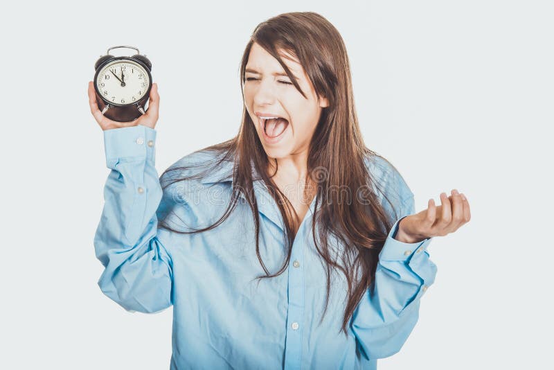Mujer joven en la camisa grande que sostiene el despertador foto de archivo Mujer joven en la camisa grande que sostiene el despertador foto de archivo