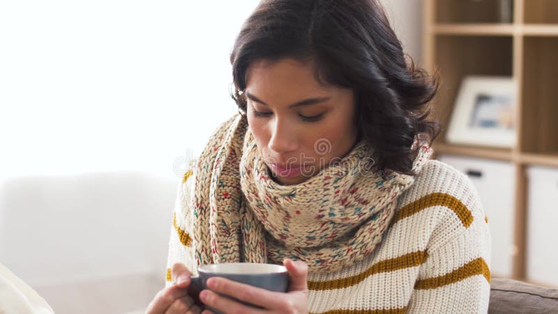 Mujer joven enferma en bufanda que bebe té caliente en casa metrajes
