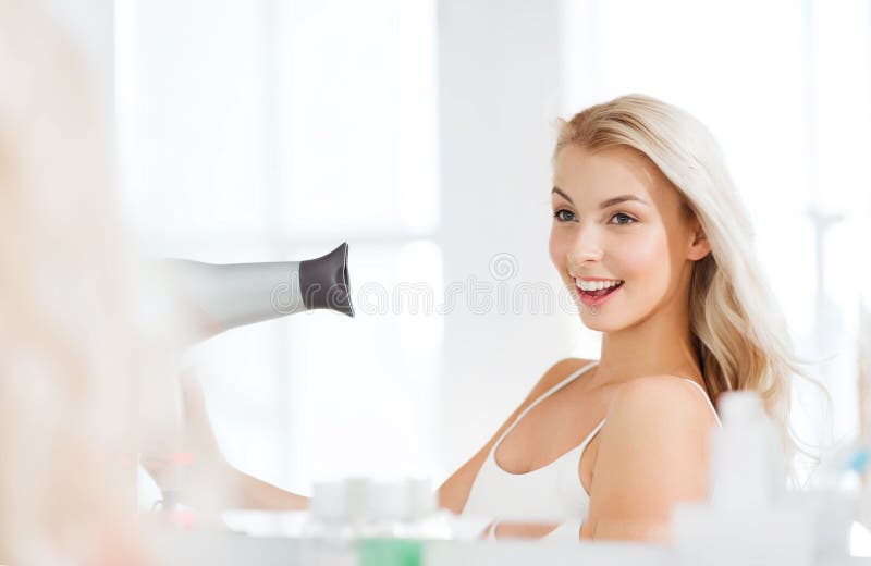 Mujer joven feliz con el cabello seco de la fan en el cuarto de baño imagen de archivo