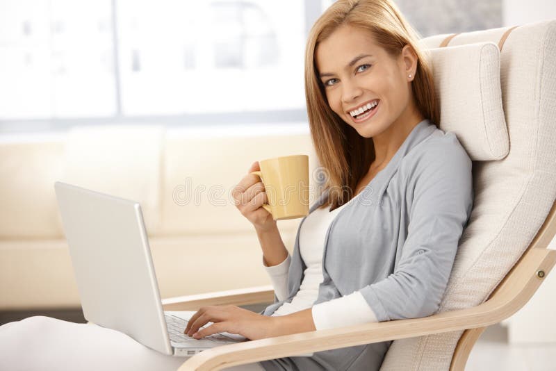 Mujer joven feliz con la taza del ordenador y de café imágenes de archivo libres de regalías Mujer joven feliz con la taza del ordenador y de café imágenes de archivo libres de regalías