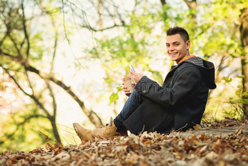 Mujer joven feliz en otoño en parque con el teléfono elegante y el café para llevar imagenes de archivo Mujer joven feliz en otoño en parque con el teléfono elegante y el café para llevar imagenes de archivo