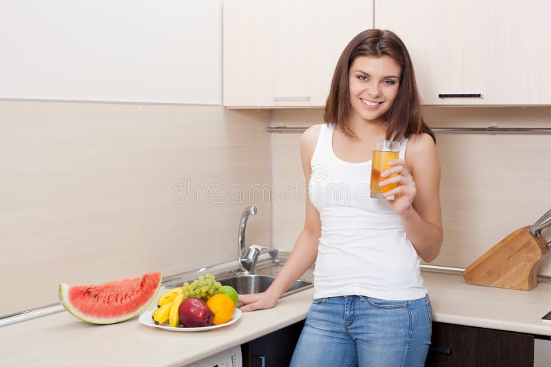 Mujer joven feliz en un jugo de consumición de la cocina foto de archivo Mujer joven feliz en un jugo de consumición de la cocina foto de archivo