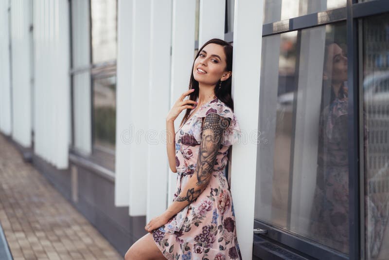 Mujer joven feliz hermosa en el vestido coloreado que presenta cerca de centro de negocios fotos de archivo libres de regalías Mujer joven feliz hermosa en el vestido coloreado que presenta cerca de centro de negocios fotos de archivo libres de regalías