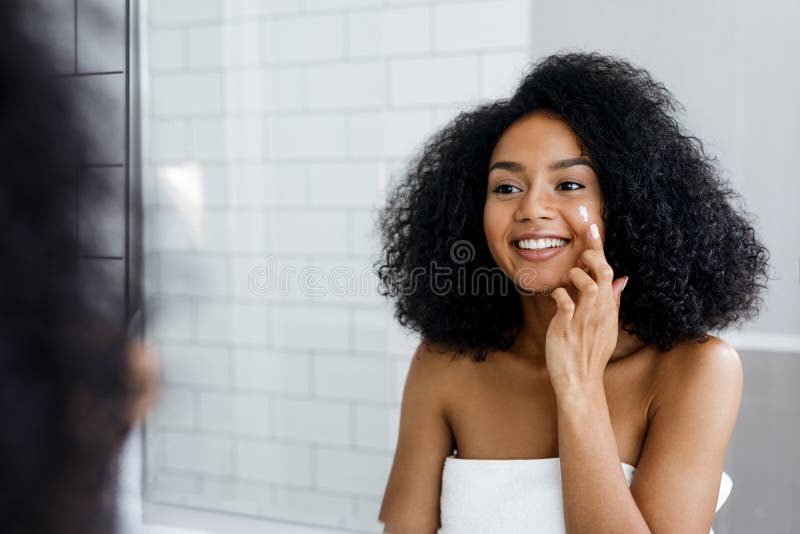 Mujer joven feliz que aplica la crema de cara imagen de archivo libre de regalías Mujer joven feliz que aplica la crema de cara imagen de archivo libre de regalías