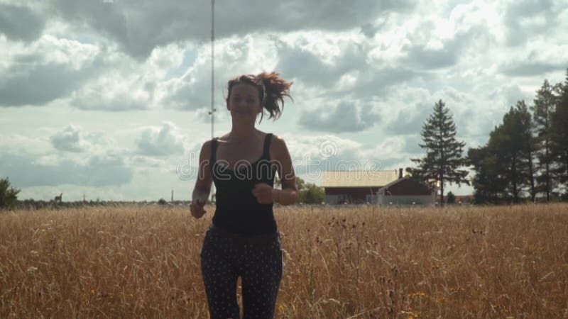 Mujer joven feliz que corre a lo largo de campo de oro en día soleado brillante