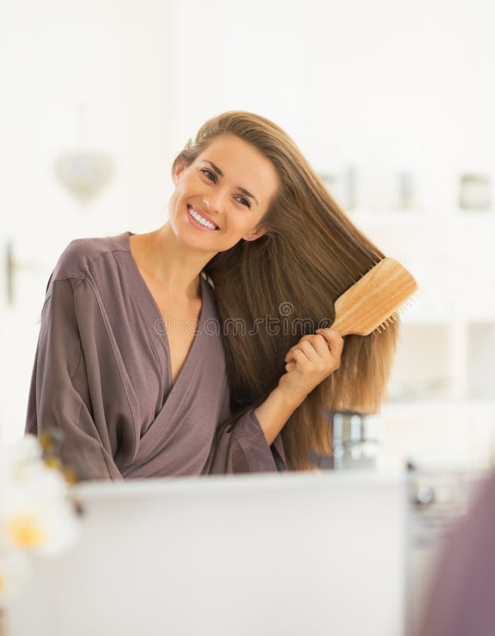 Happy young woman combing hair in modern bathroom. Happy young woman combing hair in modern bathroom