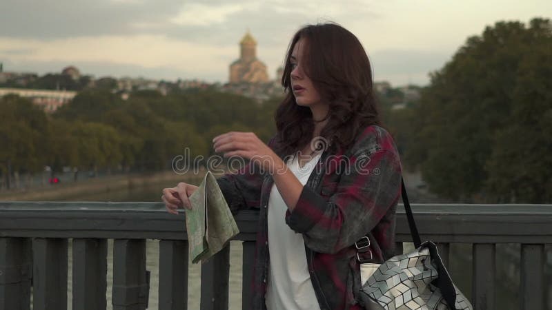 Mujer joven hermosa con el mapa turístico que mira alrededor en la calle de la ciudad