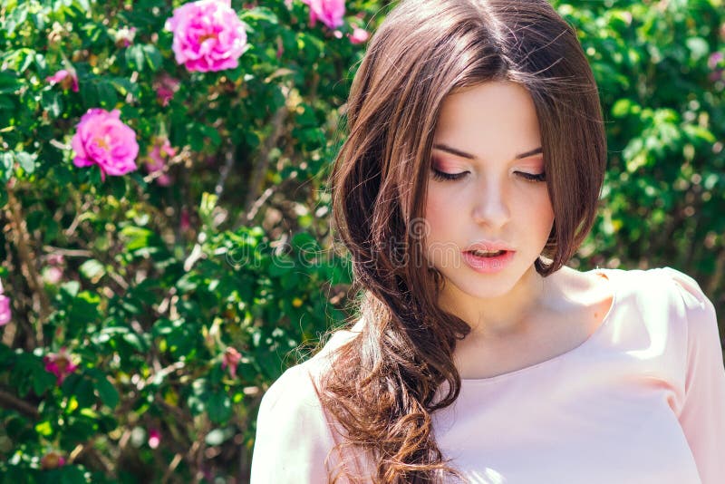 Mujer joven hermosa con el pelo rizado largo que presenta cerca de rosas en un jardín El concepto de publicidad del perfume fotos de archivo Mujer joven hermosa con el pelo rizado largo que presenta cerca de rosas en un jardín El concepto de publicidad del perfume fotos de archivo