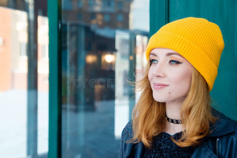 Mujer joven hermosa con el pelo rubio y los ojos azules en un sombrero que hace punto amarillo en un fondo de la pared verde fotografía de archivo libre de regalías Mujer joven hermosa con el pelo rubio y los ojos azules en un sombrero que hace punto amarillo en un fondo de la pared verde fotografía de archivo libre de regalías