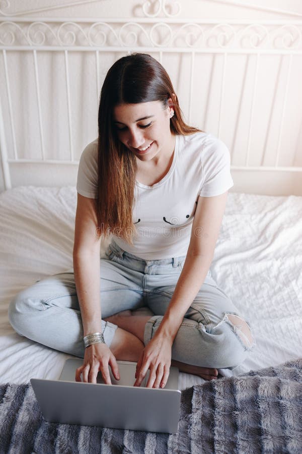 Mujer joven hermosa con los pechos dibujados en la camiseta que sonríe y que escribe en el ordenador portátil fotos de archivo Mujer joven hermosa con los pechos dibujados en la camiseta que sonríe y que escribe en el ordenador portátil fotos de archivo