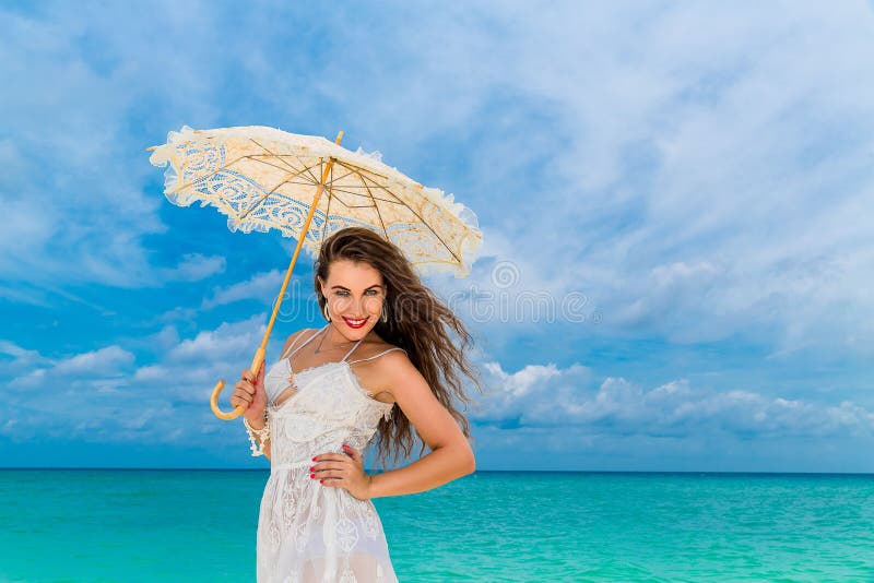 Mujer joven hermosa en el vestido blanco con el paraguas en una playa tropical imagenes de archivo Mujer joven hermosa en el vestido blanco con el paraguas en una playa tropical imagenes de archivo