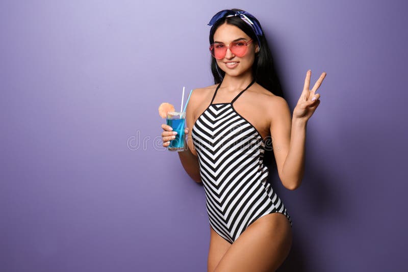 Mujer joven hermosa en traje de natación y con la bebida en fondo del color fotografía de archivo libre de regalías Mujer joven hermosa en traje de natación y con la bebida en fondo del color fotografía de archivo libre de regalías