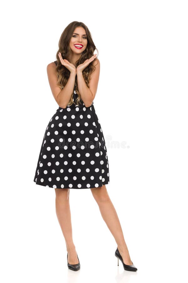 Mujer joven hermosa en vestido de cóctel negro en las manos y la sonrisa de Dots Is Holding Head In de la polca imágenes de archivo libres de regalías Mujer joven hermosa en vestido de cóctel negro en las manos y la sonrisa de Dots Is Holding Head In de la polca imágenes de archivo libres de regalías