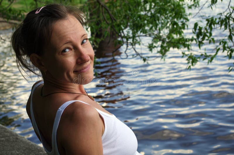 Mujer joven hermosa feliz que sonríe y que mira la cámara, agua cercana permanente en el lago fotografía de archivo Mujer joven hermosa feliz que sonríe y que mira la cámara, agua cercana permanente en el lago fotografía de archivo