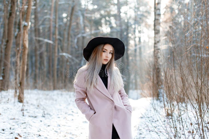 Mujer joven hermosa linda con el pelo rubio en un sombrero negro elegante del vintage en una capa elegante rosada que presenta en foto de archivo Mujer joven hermosa linda con el pelo rubio en un sombrero negro elegante del vintage en una capa elegante rosada que presenta en foto de archivo