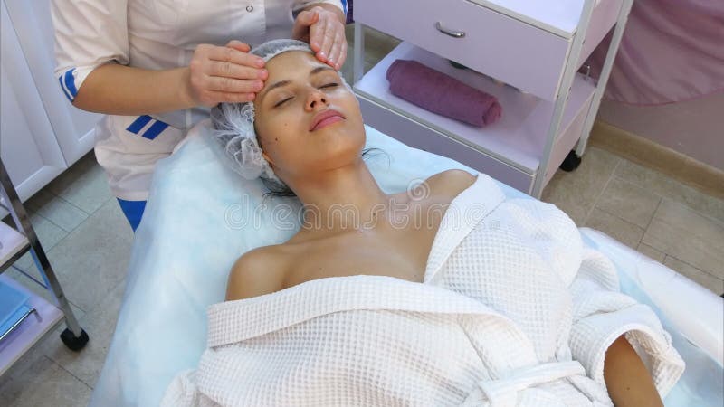 Mujer joven hermosa que recibe masaje facial con los ojos cerrados en un salón del balneario