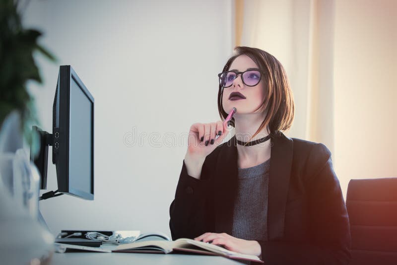 Mujer joven hermosa que se sienta en el escritorio y que piensa en el co foto de archivo Mujer joven hermosa que se sienta en el escritorio y que piensa en el co foto de archivo