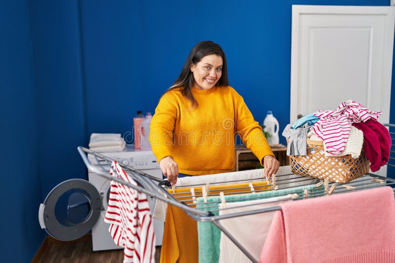 Mujer joven, hermosa y grande, sonriente y segura colgando ropa en la lavandería imagen de archivo libre de regalías