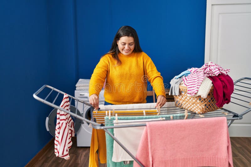 Mujer joven, hermosa y grande, sonriente y segura colgando ropa en la lavandería fotografía de archivo libre de regalías