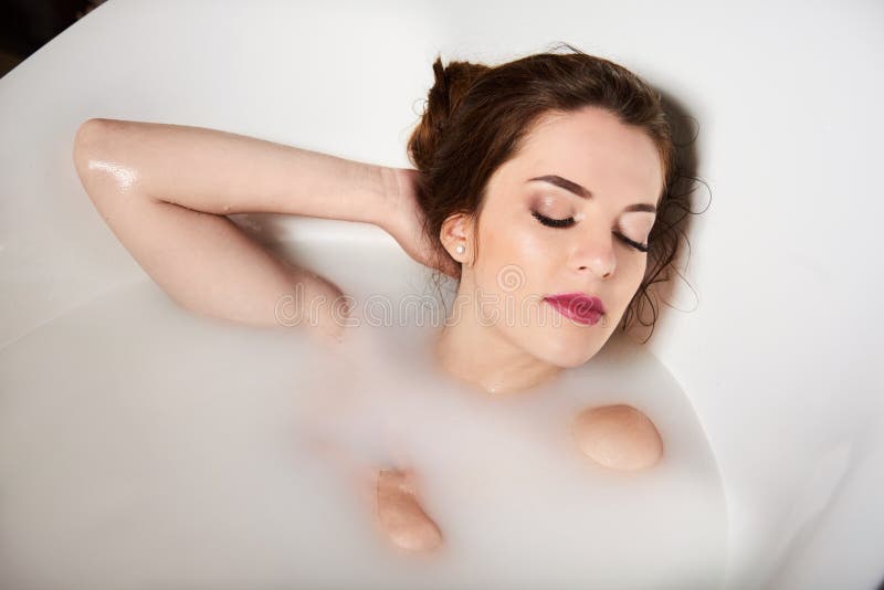 Mujer joven linda que sonríe en tina de baño por completo de leche imágenes de archivo libres de regalías Mujer joven linda que sonríe en tina de baño por completo de leche imágenes de archivo libres de regalías