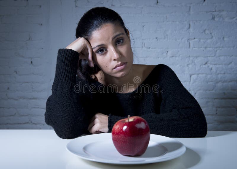 Young woman or teen looking apple fruit on dish as symbol of crazy diet in nutrition disorder concept anorexia and bulimia and refusing to eat food in diet calories obsession. Young woman or teen looking apple fruit on dish as symbol of crazy diet in nutrition disorder concept anorexia and bulimia and refusing to eat food in diet calories obsession