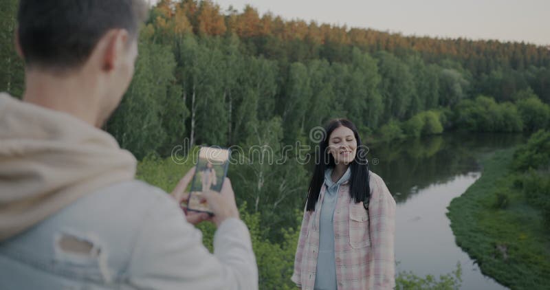 Mujer joven posando para la cámara mientras un hombre toma una foto con un smartphone al aire libre en un parque nacional con mont